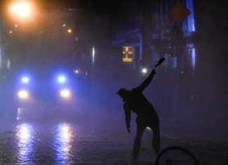 18 Monate Haft auf Bewährung für G20-Randalierer Eine schwarz gekleidete Person ist von hinten zu sehen, wie sie im Dunkeln mit einer Flasche schmeißt.