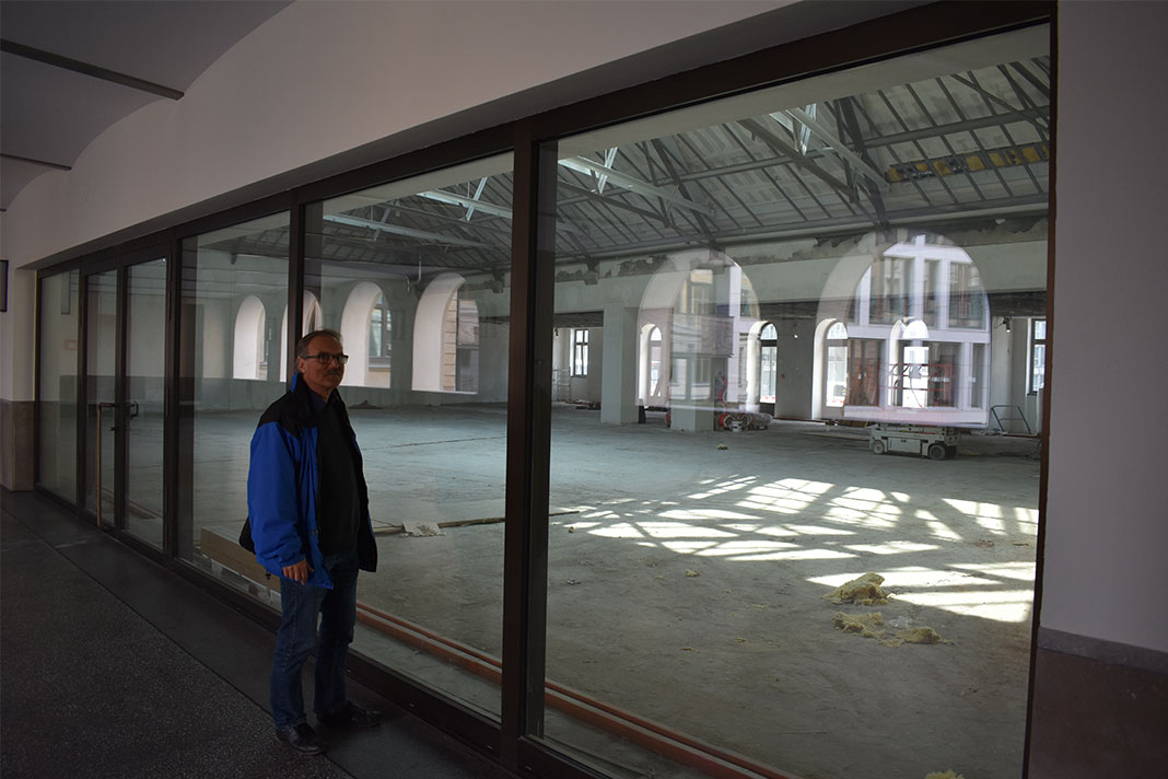 Ein Mann steht vor einer Fensterscheibe, hinter der ein großer leerer Raum ist.