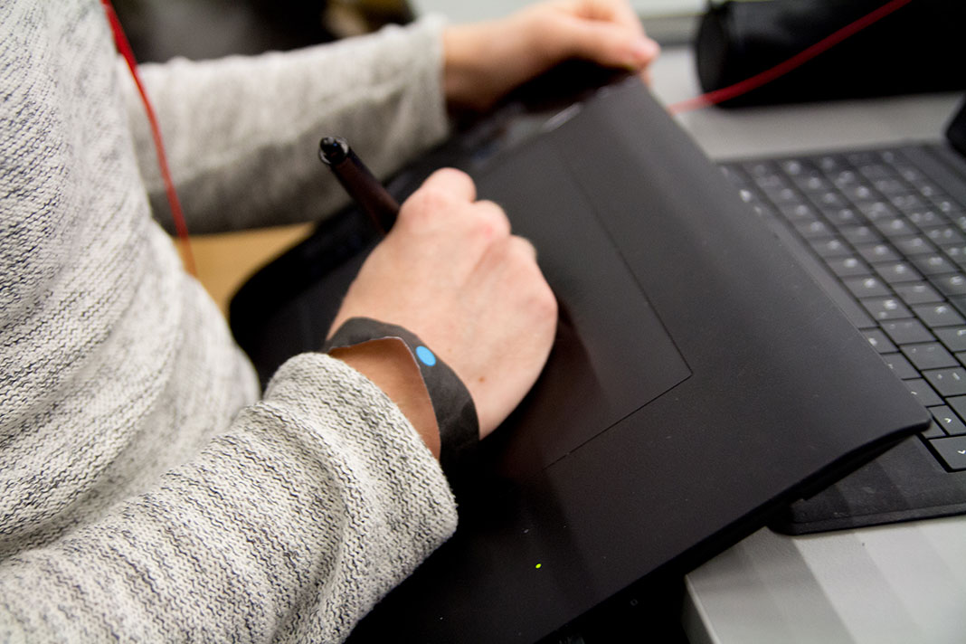 Ein Teilnehmer des HAW Game Jam zeichnet auf seinem Grafik-Tablet. Am Arm trägt er ein Armband mit blauem Punkt.