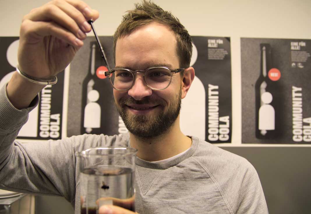 Jan van Schwamen tropft Zuckerkulör für die Community Cola in ein Glas mit Wasser.