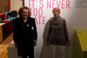 Die beiden Senior-Guides Barbara Greulich und Ute Zäpernick stehen in der Ausstellung vor einer Wand mit dem Schriftzug "It's never too late".
