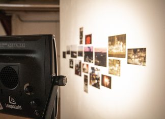 “Design ist angewandt. Kunst wird interpretiert.” Eine Fotowand mit Scheinwerfern beschienen.