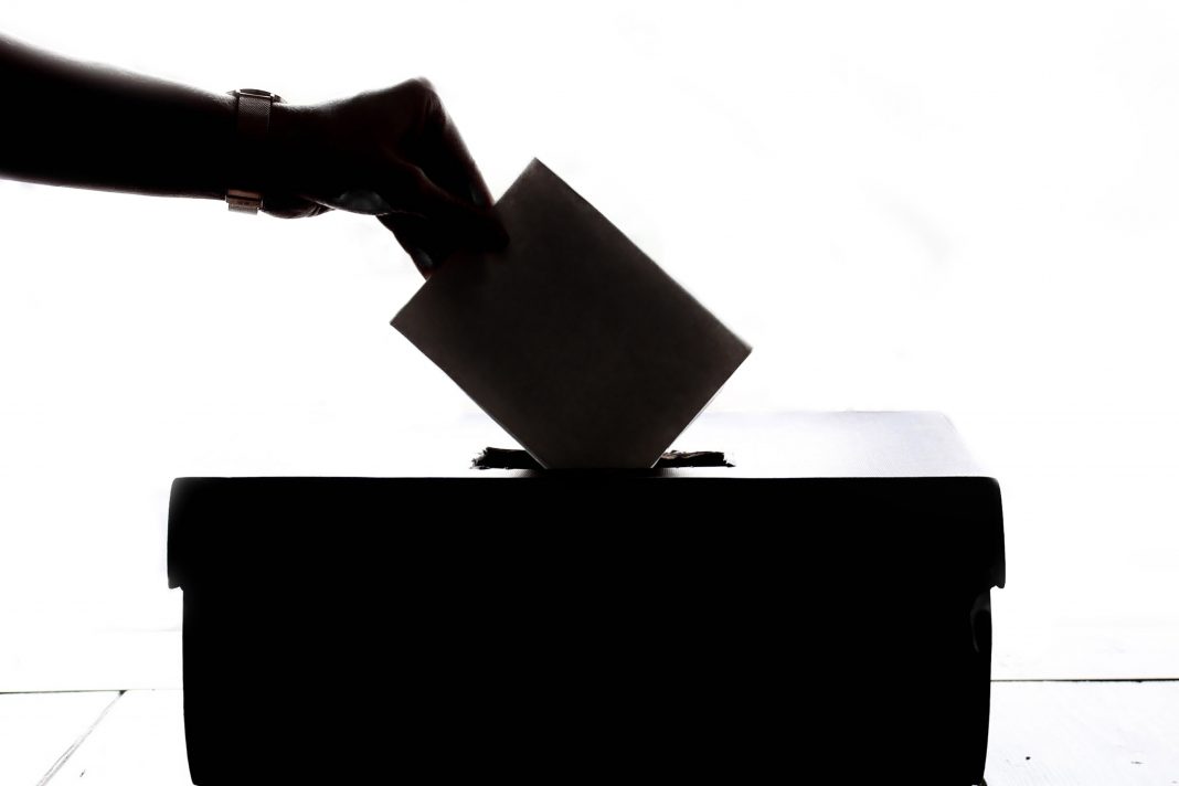 Hand, die Wahlbrief in Wahlurne steckt