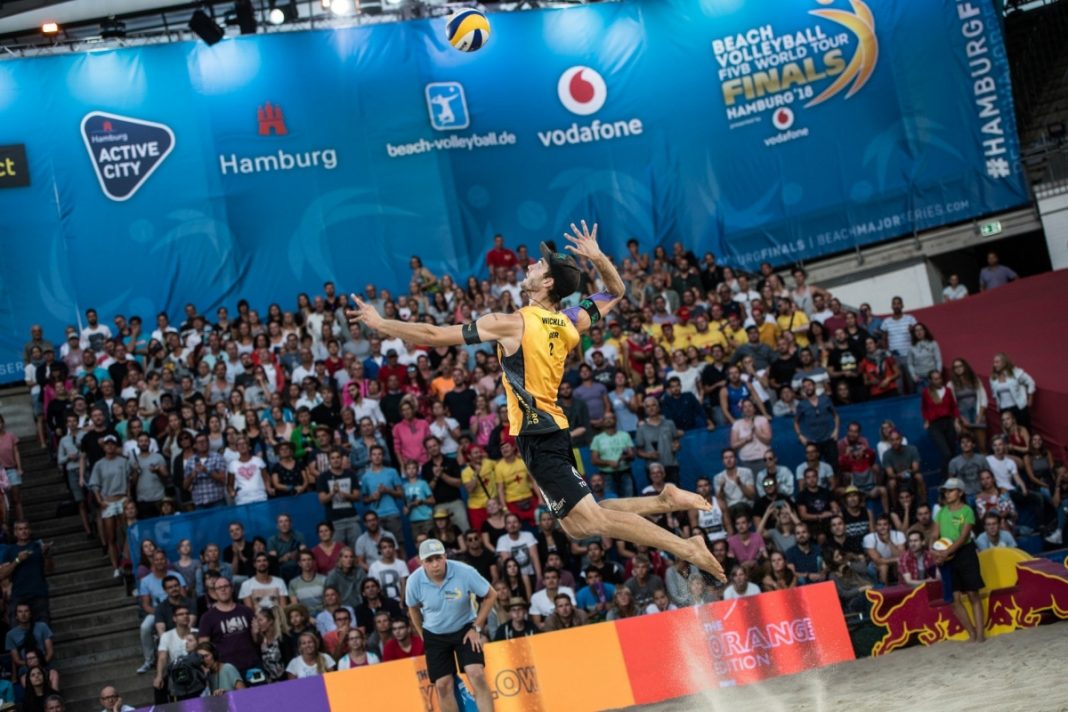 Ein Volleyballer ist im Sprung in der Luft und setzt zum Aufschlag an. Im Hintergrund sind Fans auf einer Tribüne.