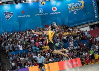 Beachvolleyball-WM startet in Hamburg Ein Volleyballer ist im Sprung in der Luft und setzt zum Aufschlag an. Im Hintergrund sind Fans auf einer Tribüne.