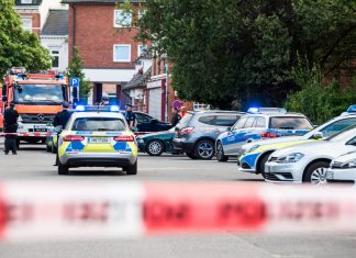 Tödliche Schüsse in Lohbrügge Polizisten und Feuerwehrleute stehen am Tatort in Lohbrügge. Vorne ist ein Absperrband zu sehen.