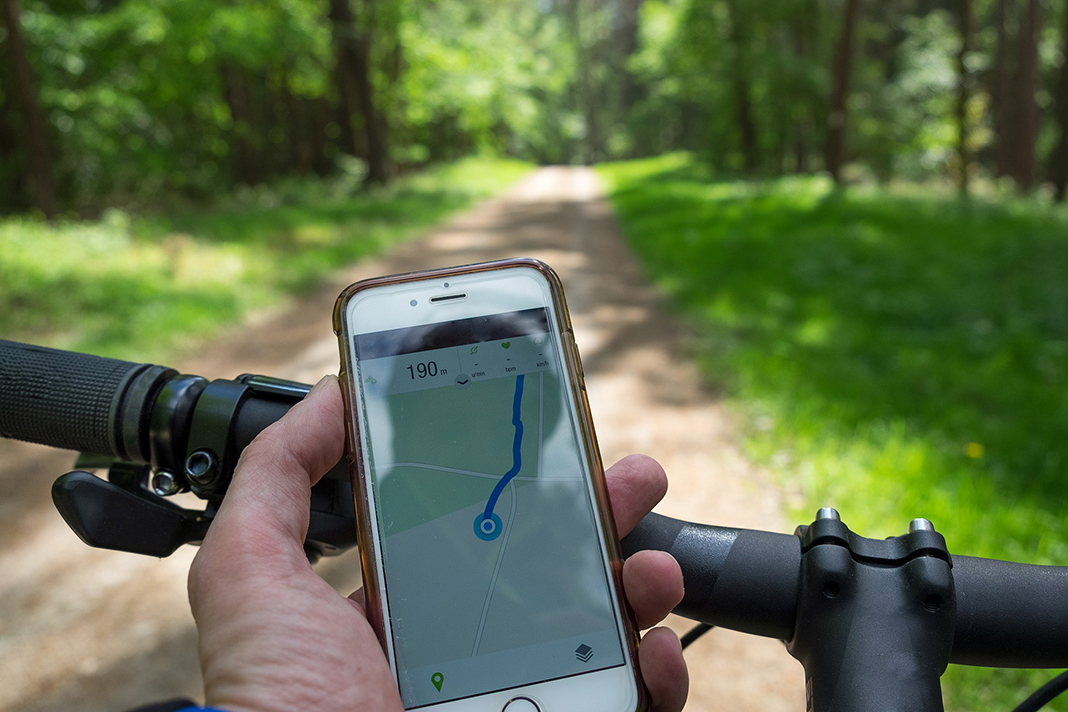 Eine Hand hält eine Handy in der Hand, während der Fahrt auf einem Fahrrad.