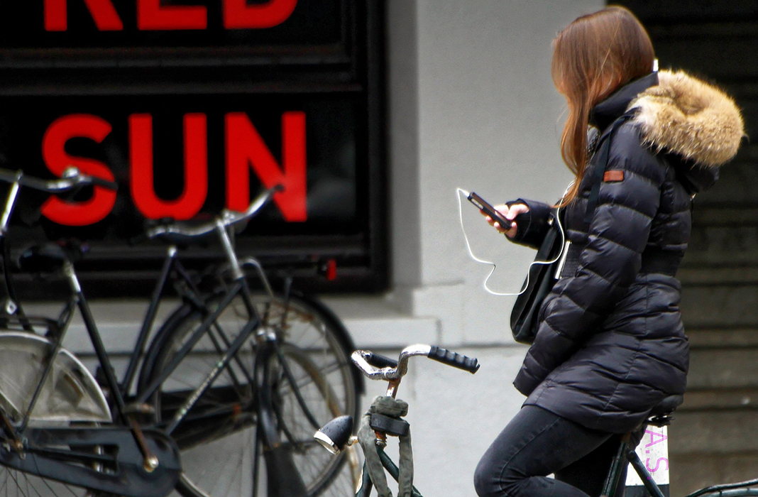 Eine Frau hält ihr Smartphone in der Hand und sitzt auf ihrem Fahrrad.