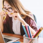 Macht Abi, aber macht euch locker Frau sitzt vor ihrem Laptop und beißt auf einen Stift