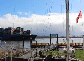 Ein Stück Seemannskultur im Hamburger Hafen Blauer Containerfrachter fährt die Elbe entlang, im Vordergrund Biergarten der Schiffsbegrüßungsanlage Willkomm Höft.