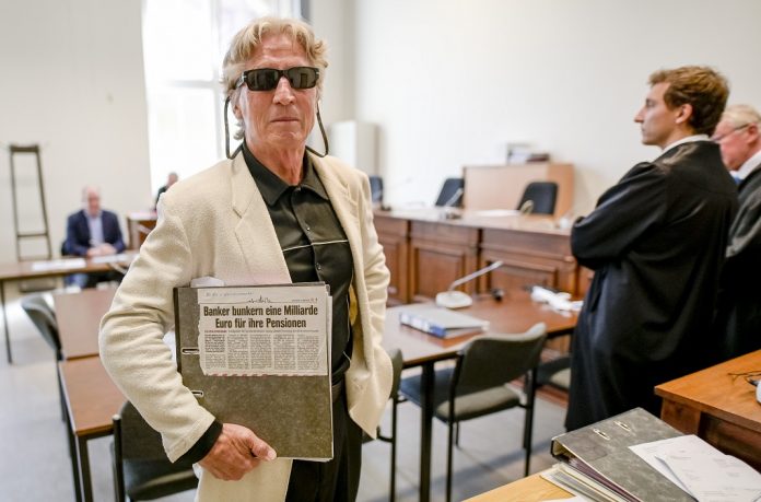 70-Jähriger mutmaßlicher Serienbankräuber steht im Gericht und hält einen Zeitungsartikel.