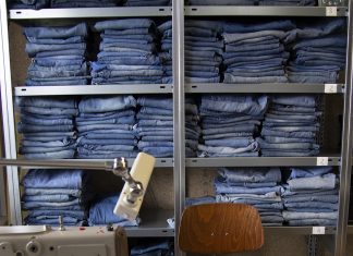 “Deutschland ist einfach krass zeugnisverliebt” Gestapelte blaue Jeans im Regal, davor eine Nähmaschine