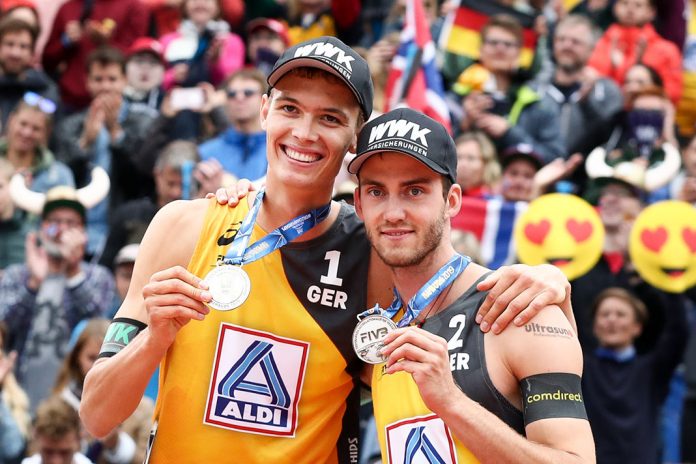 Beachvolleyball-Vizemeister Julius Thole und Clemens Wickler mit ihren Silbermedaillen, im Hintergrund feiernde Fans