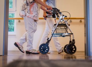 Mehr Personal in den Pflegeberufen Ältere Frau geht mit einem Rollator und einem Pfleger über den Gang.