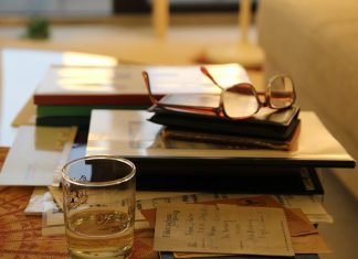 Fachkräftemangel an Hamburger Universitäten Eine Brille liegt auf einem Buch. Davor steht ein Glas mit einer Flüssigkeit bis zur Hälfte gefüllt.