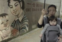 Ein Kind – so will es der Staat Nanfu Wang mit ihrem Kind vor einer Wand mit chinesischer Ein-Kind-Propaganda: "One Child is best"