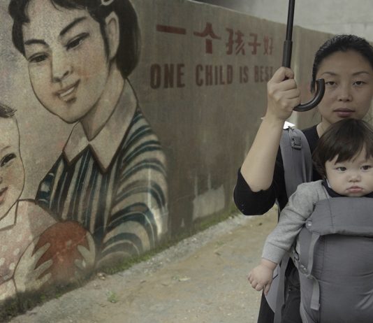 Ein Kind – so will es der Staat Nanfu Wang mit ihrem Kind vor einer Wand mit chinesischer Ein-Kind-Propaganda: "One Child is best"