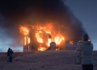 Island als Wimmelbild Eine Scheune brennt im Schnee. Leute schauen gebannt zu.
