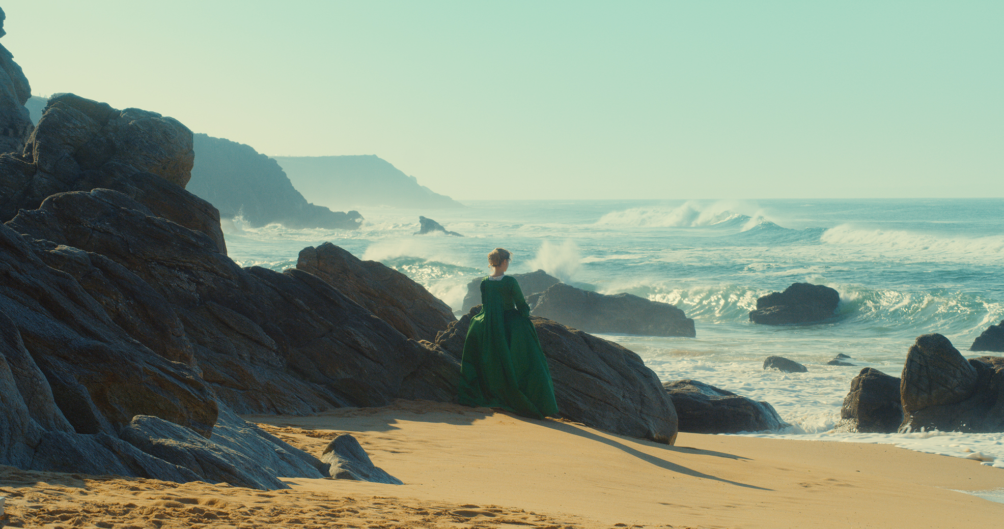 Frau in langem, barocken Kleid steht am Strand