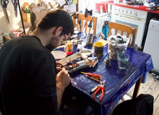 Reparieren statt wegwerfen im Repair Café Mann repariert und schraubt an einem Draht. Auf seinem Tisch herrscht Chaos.