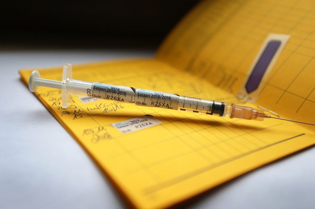 Eine Spritze die mit dem Namen des Vierfach-Grippeimpfstoff Influvac Tetra gekennzeichnet ist, liegt auf einem Impfpass.