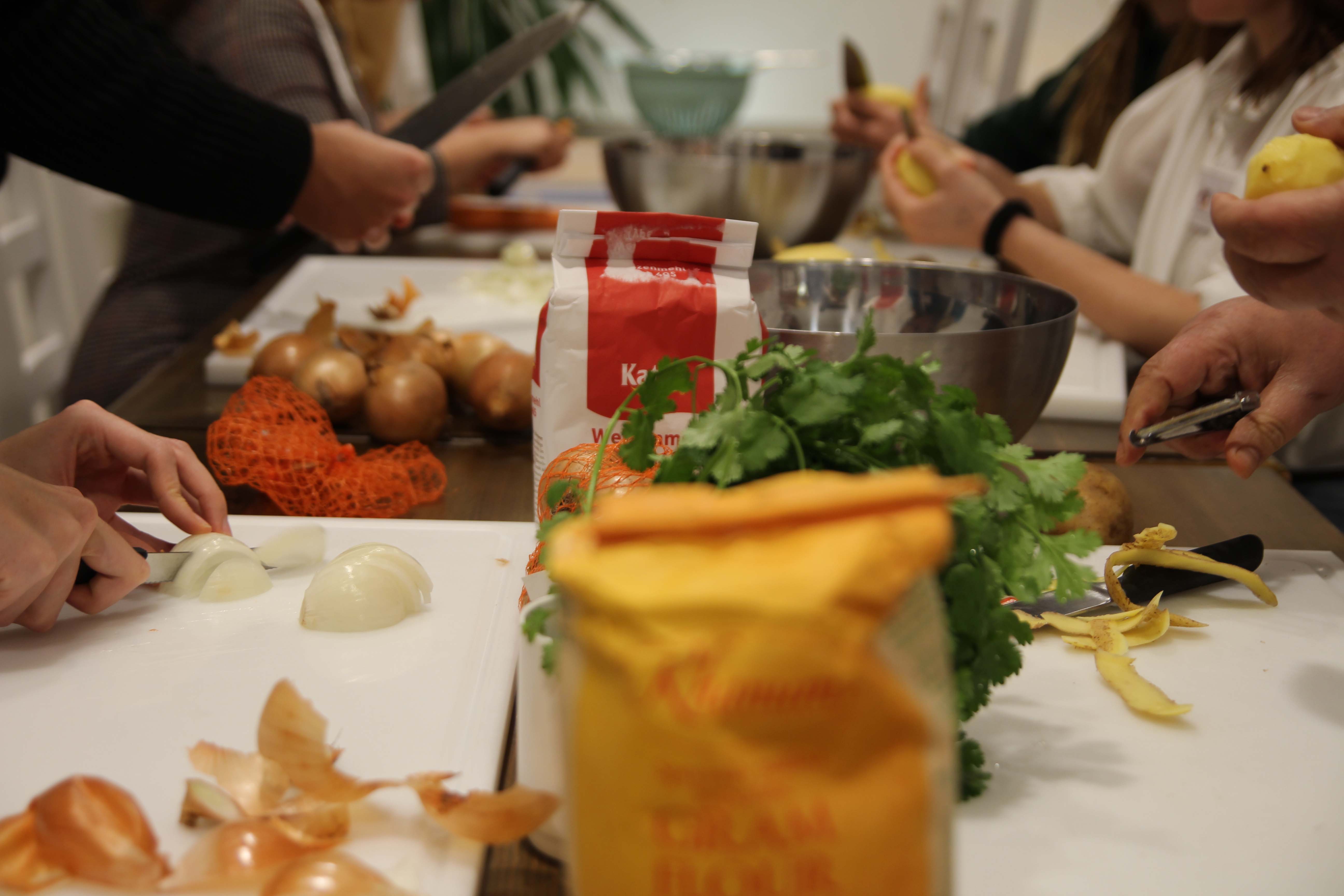 Ein langer Tisch mit verschiedenen Zutaten, wie Zwiebeln und Tomaten, die von vielen Händen geschnitten werden.