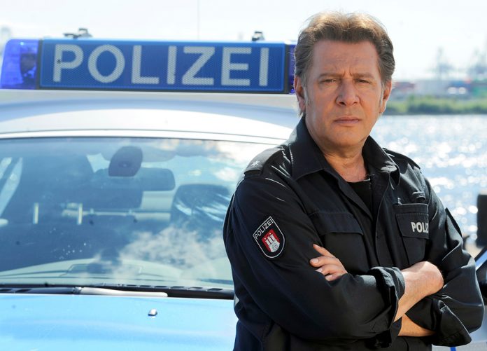 Jan Fedder steht vor einem Polizeiwagen in Hamburg.