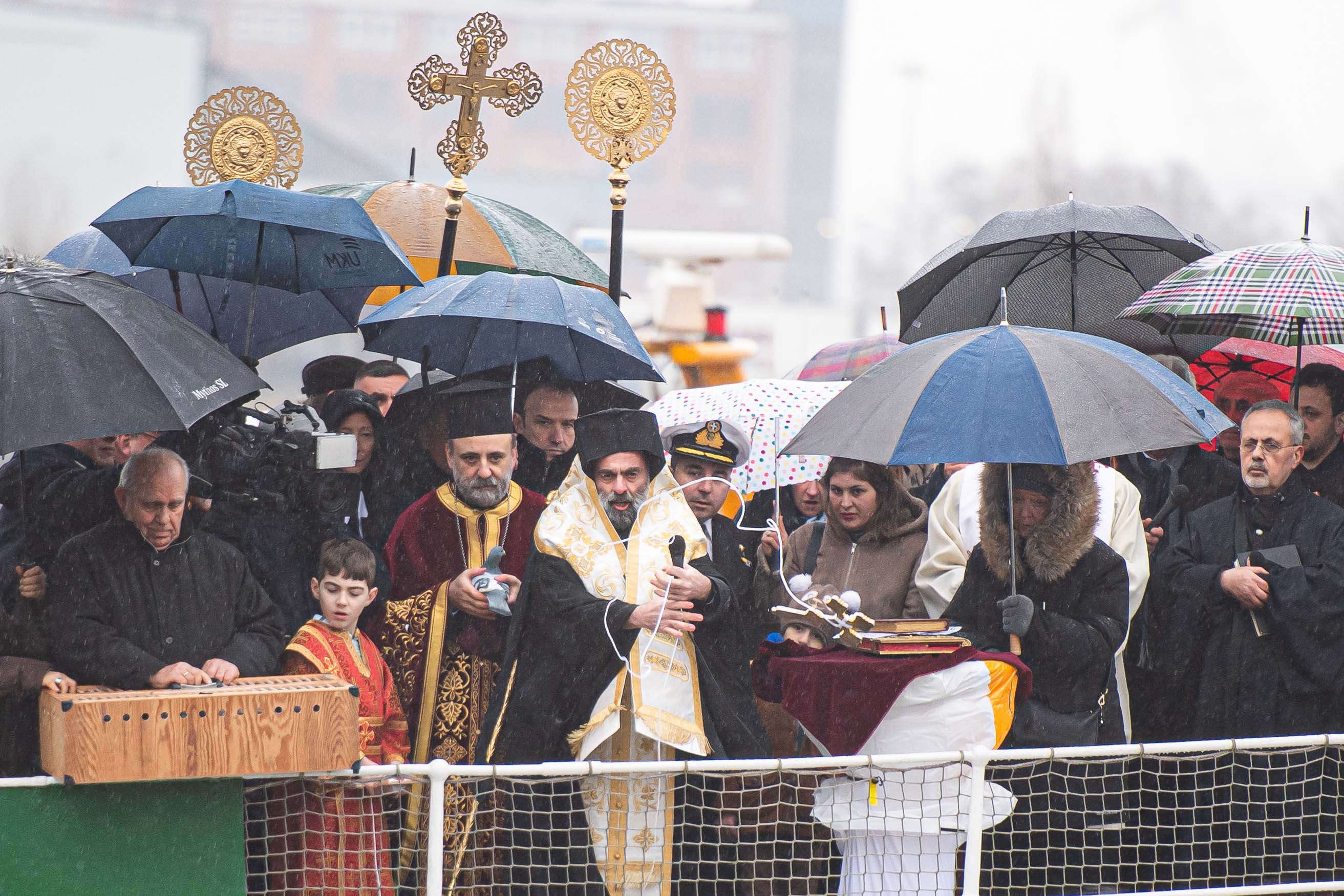 Grieschisch-orthodoxer Bischof segnet an Bord eines Schiffs das Wasser der Elbe, umringt von Menschen mit Regenschirmen.