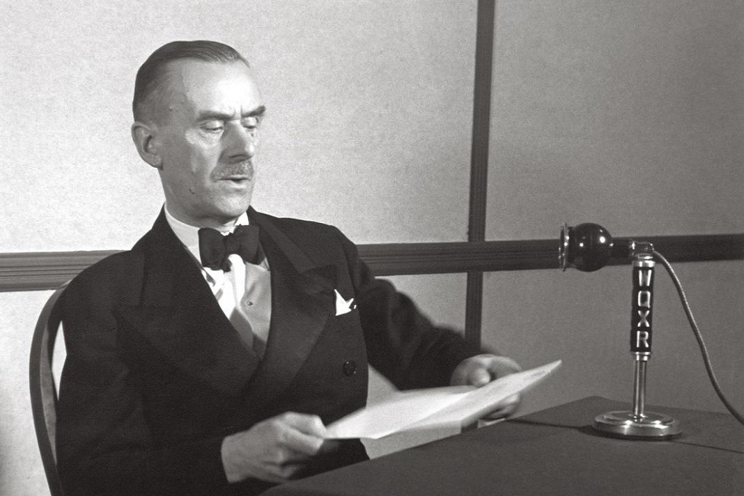 Thomas Mann sitzt mit einem Schriftblatt vor einem Mikrofon. Foto: Eric Schaal / Weidle Verlag