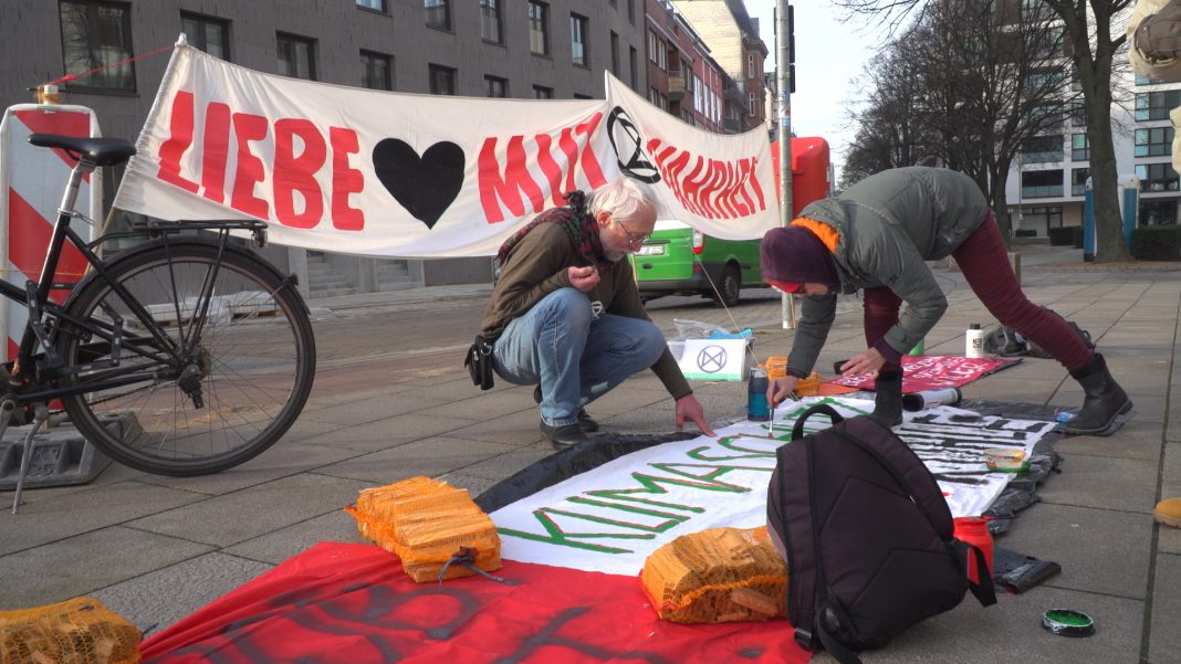 Zwei Menschen bemalen einen Banner vor dem Siemens-Gebäude in Hamburg.