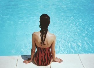 Warum ich ins Freibad gehe, obwohl ich es eigentlich hasse Eine Frau sitzt am Beckenrand eines Schwimmbeckens, Symbolbild.