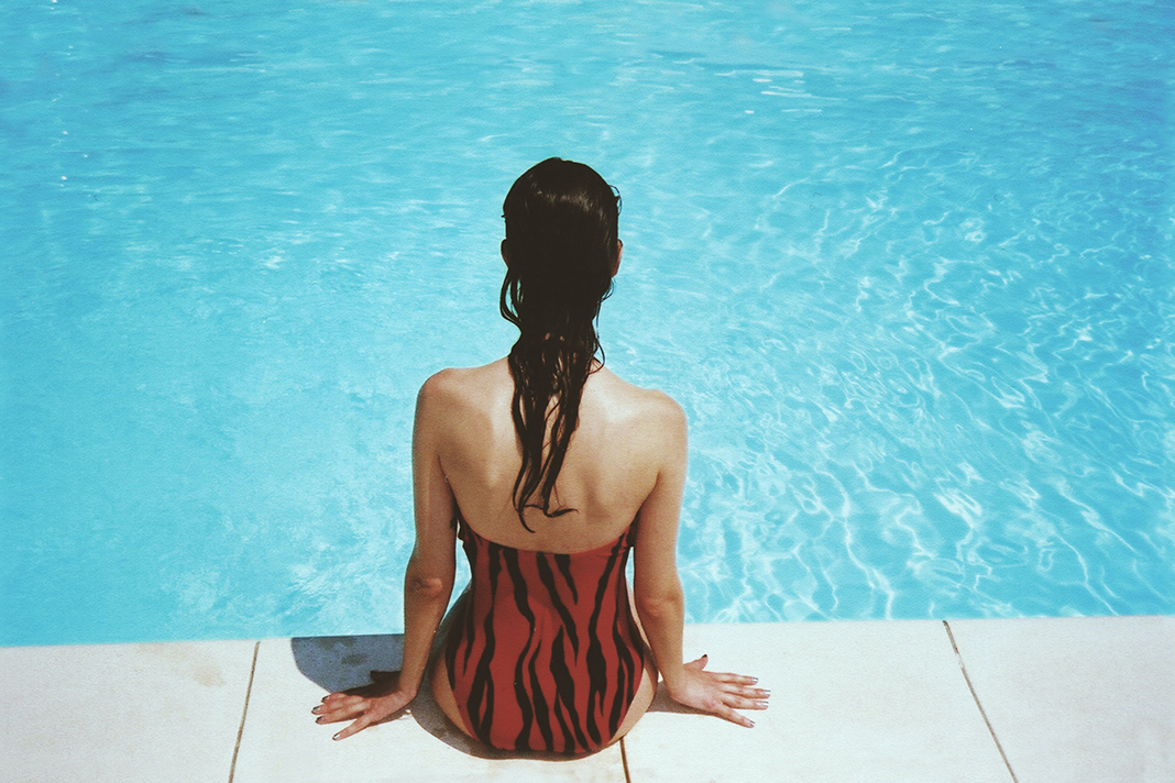 Eine Frau sitzt am Beckenrand eines Schwimmbeckens, Symbolbild.