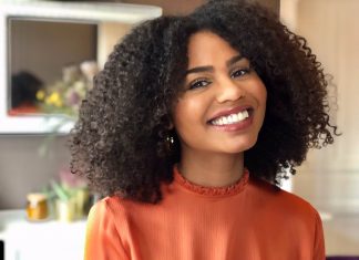 Afrohaare: Zwischen Pflege und Empowerment Afrohaare Portraitfoto von Abina Ntim. Sie trägt ihre gelockten, schulterlangen Afohaare offen und lächelt.