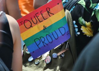Kostenlose Ferienangebote für queere Jugendliche Regenbogenflagge, auf der Queer & Proud steht in einem Rucksack.