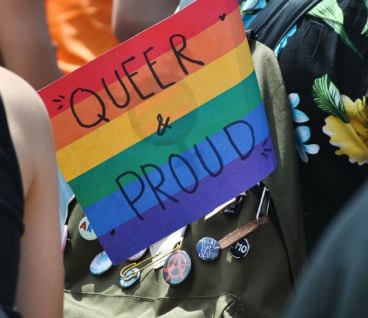 Kostenlose Ferienangebote für queere Jugendliche Regenbogenflagge, auf der Queer & Proud steht in einem Rucksack.