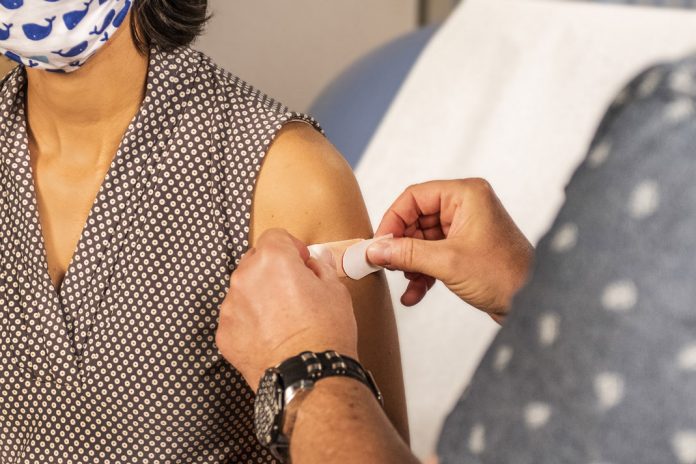 Corona Impfung: Frau bekommt Pflaster auf Arm geklebt nach einer Impfung.