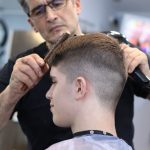 Senat weitet 2G-Regel auf Friseure und andere Geschäfte aus Ein Friseur schneidet einem Jugendlichen die Haare. Beide tragen keine Maske. Ab Samstag wil der Senat das Friseuren wieder erlauben.