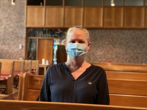 Eine Frau mit Maske sitzt in einer Kirche und ruht sich nach der Impfung aus.