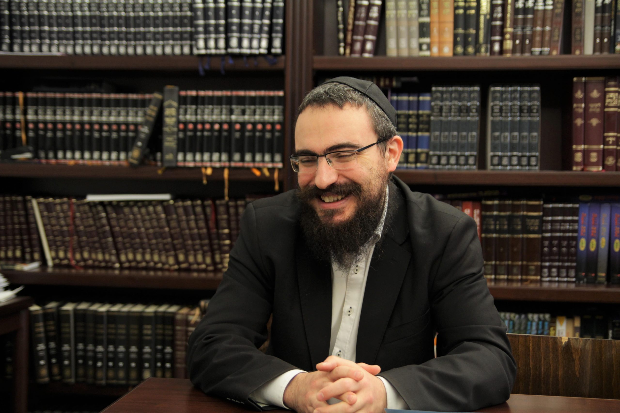 Rabbiner Arye Merkhasin vom Chabad Hamburg sitzt vor einer Wand aus Büchern.