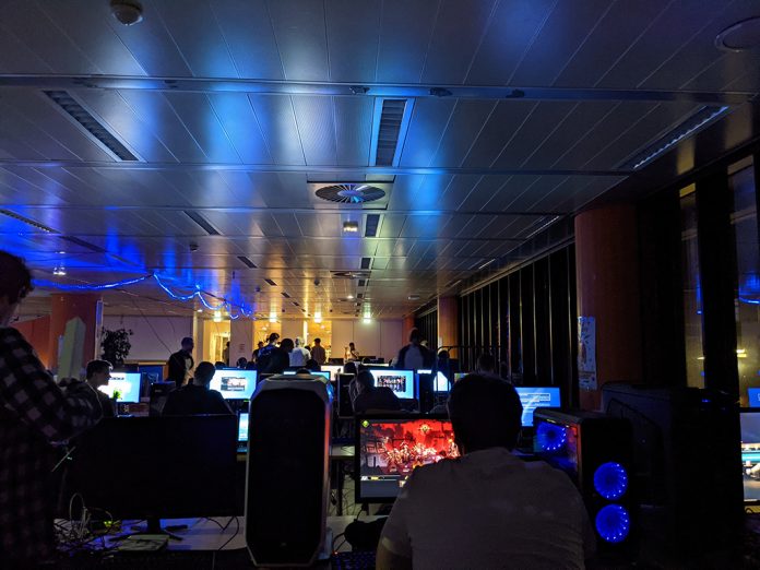 HAW LAN-Party 2021 am Berliner Tor. Der Raum ist dunkel und beleuchtet mit Neon-Lichtern. Einige Menschen sitzen vor PCs und spielen Videospiele