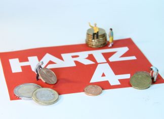 2021 weniger Menschen auf Sozialhilfe angewiesen Miniaturfiguren spielen mit Euromünzen. Zwei Figuren heben eine Centmünze hoch, eine sitzt auf einem Stapel Münzen. Auf dem roten Boden unter den Münzen steht „Hartz 4“. Das Bild steht symbolisch für Menschen, die Sozialhilfe beziehen.