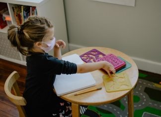 Corona in Kitas: Ausweitung der Teststrategie Ein Kind mit Mund-Nase-Schutz spielt am Tisch. Foto: Unsplash