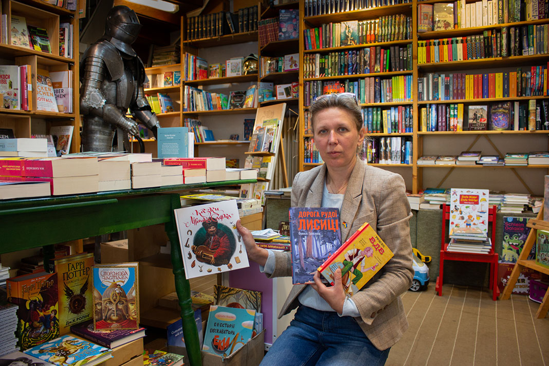 Buchhändlerin Natalia Banakh sitzt auf einem Stuhl und zeigt ukrainische Bücher