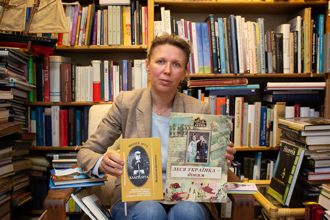 Buchhändlerin Natalia Banakh sitzt auf einem Stuhl und zeigt ukrainische Bücher