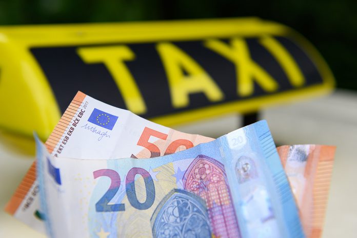 Taxifahren in Hamburg wird teurer. Geldscheine vor einem Taxi-Schild.
