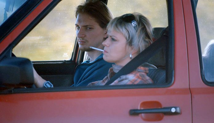 Ukrainischer Film My Thoughts Are Silent. Man sieht einen jungen Mann und eine Frau mit Zigarette im Mund in einem roten Auto sitzen.
