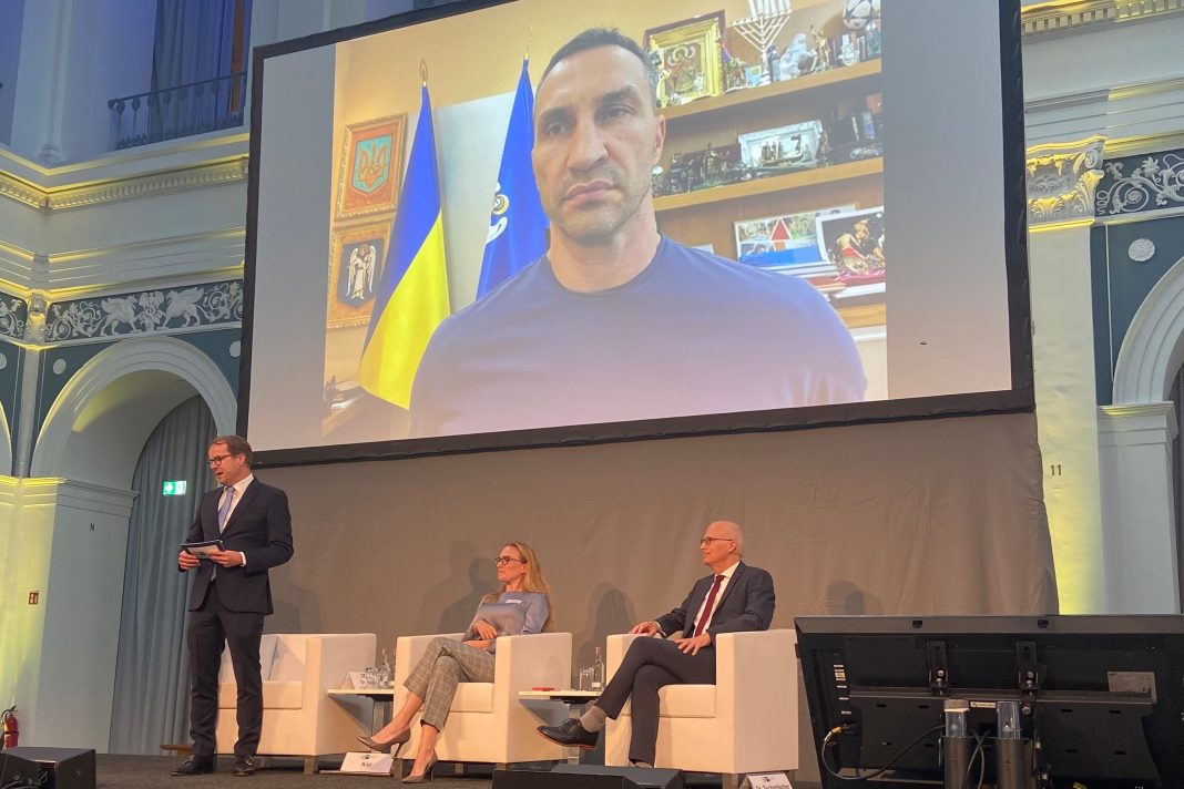 Pakt Hamburg Kiew ist das Diskussionsthema. Im Börsensaal der Handelskammer Hamburg. Wladimir Klitschko ist live auf einer großen Leinwand zugeschaltet. Auf der Bühne sitzen Peter Tschentscher, Tatjana Kiel und Malte Heyne.