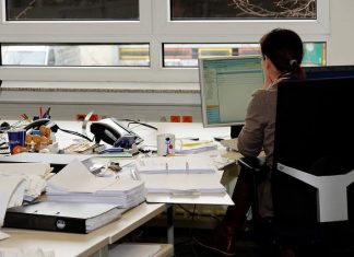 Zahl der Arbeitslosen in Hamburg steigt Arbeitslos Hamburg: Eine Frau mit dunklen Haaren sitzt an einem Schreibtisch und arbeitet am Computer. Auf dem Schreibtisch herrscht Chaos. Es liegen Papiere, Ordner und andere Arbeitsmaterialien herum.