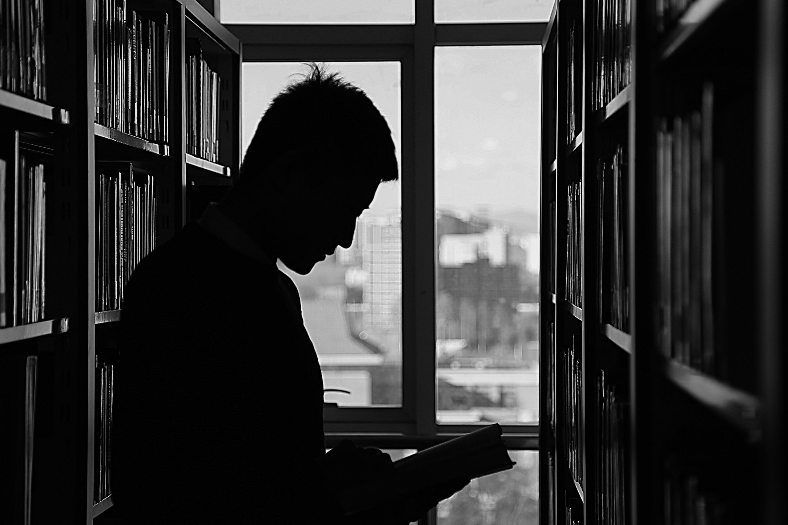 Silhouette Mann steht zwischen Bücherregalen und liest. Bücherhallen Hamburg FlexiBib (Symbolbild). Foto: Pexels