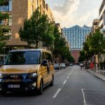Sammeltaxis fahren ab 2023 in mehr Stadtteilen Ein goldenes Moia Sammeltaxi auf einer Straße in Hamburg. Im Hintergrund sieht man die Elbphilharmononie. Foto: Moia